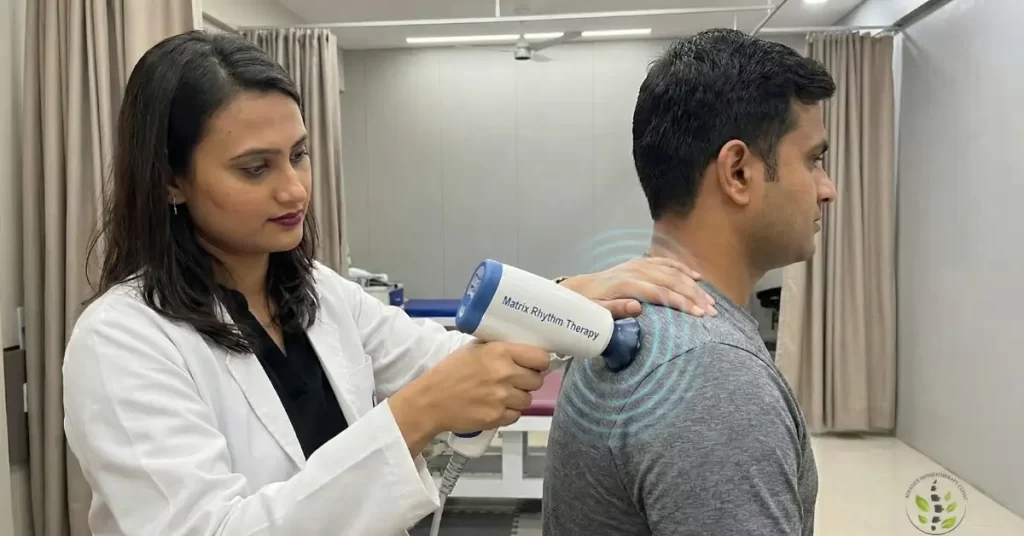 A close-up view of a physiotherapist using a Matrix Rhythm Therapy (MRT) handheld device on a patient's shoulder muscle to restore cellular oscillation.
